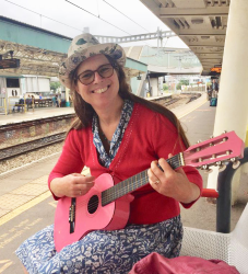 Colour photo of Lizzy Lister playing the guitar at a train station